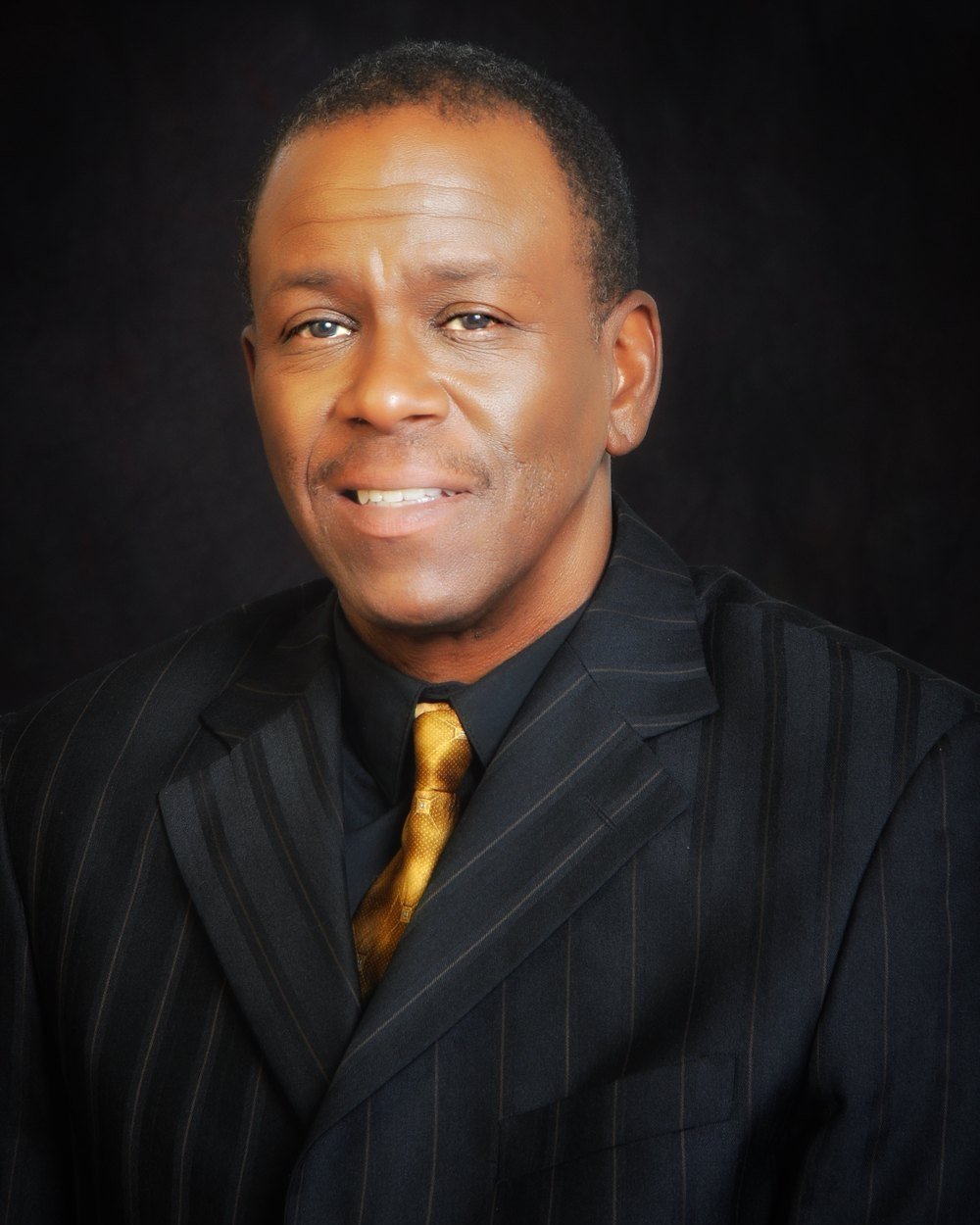 Formal headshot of Robert Reddrick in a pinstripe suit and gold tie