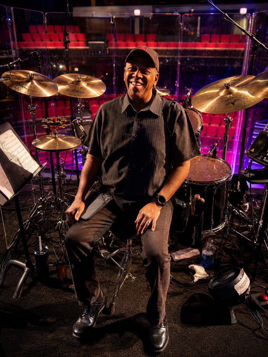 Robert Reddrick smiling behind his drum kit in the orchestra pit of a theater